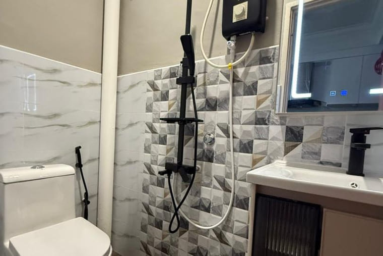 A completed bathroom with a grey-and-white geometric feature tile band, a wall-hung vanity with a fluted cabinet front, a backlit mirror, a black rain-shower column and a linear drain.