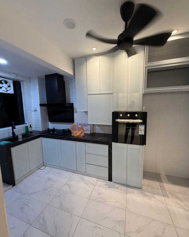 A kitchen with an L-run of white slab-front cabinets and tall units, a black worktop, a black chimney cooker hood and a built-in oven.